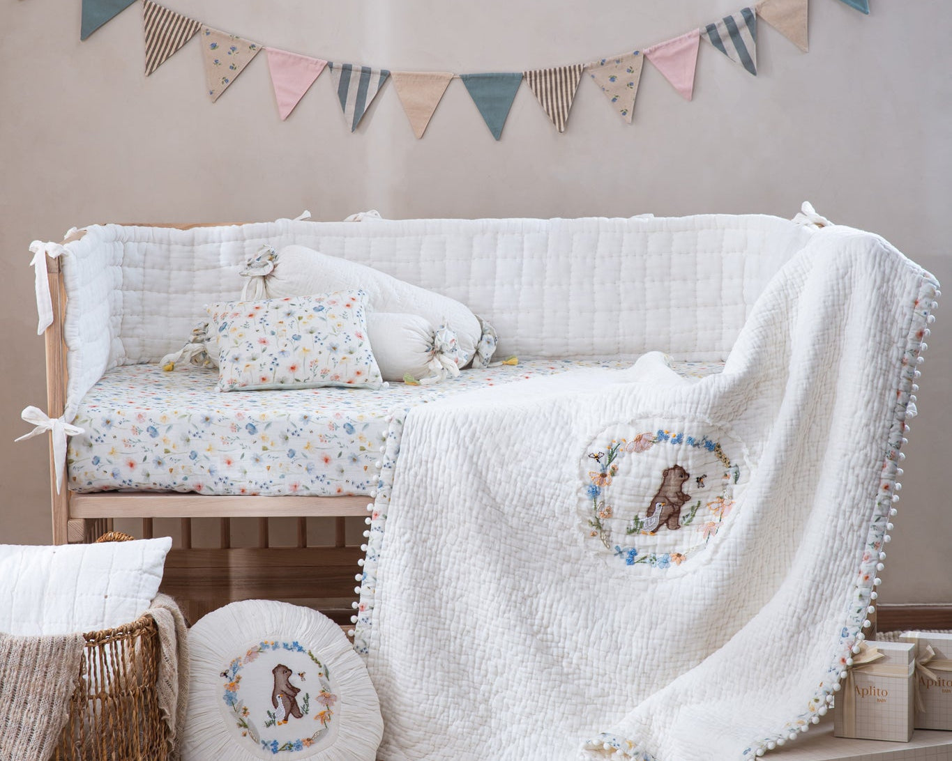 Aplito Bear and Bloom bedding with a bear-motif quilt and floral pillows displayed on a wooden cot.