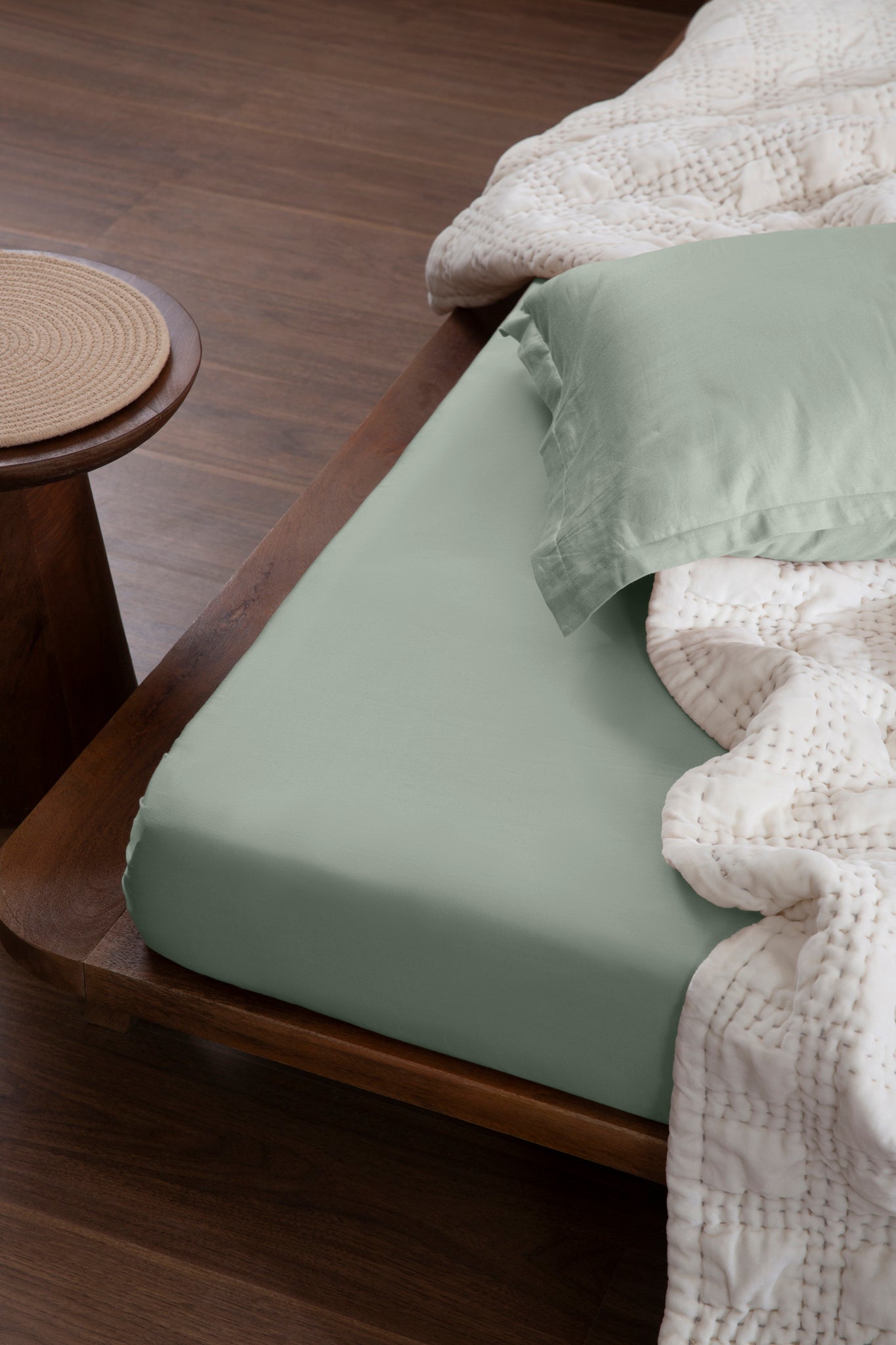 Aplito sage-green sheet and matching pillow cover on a wooden bed with an off-white quilt.