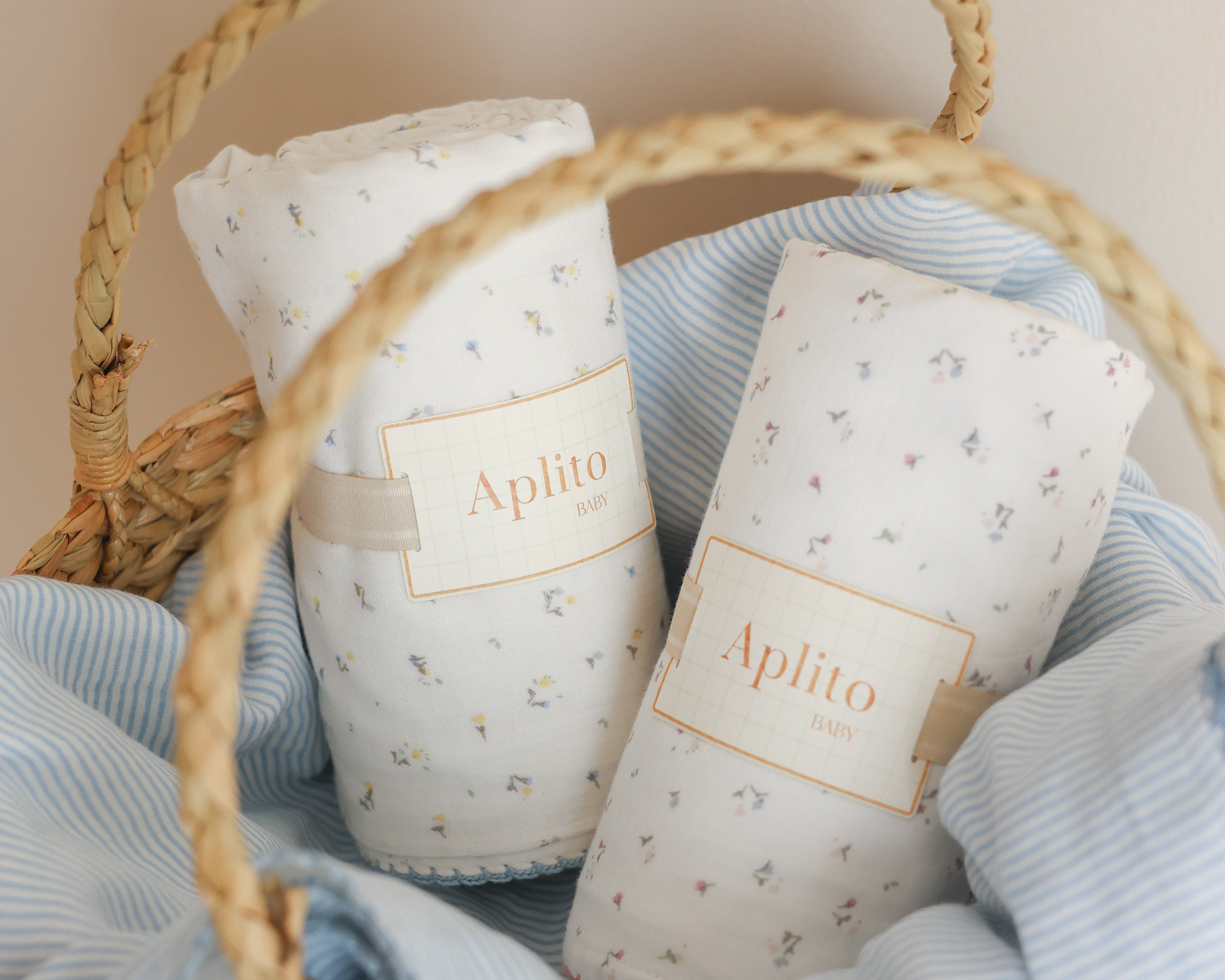 Aplito Sweet Haven in Blue swaddles rolled in a woven basket lined with pale blue striped fabric.
