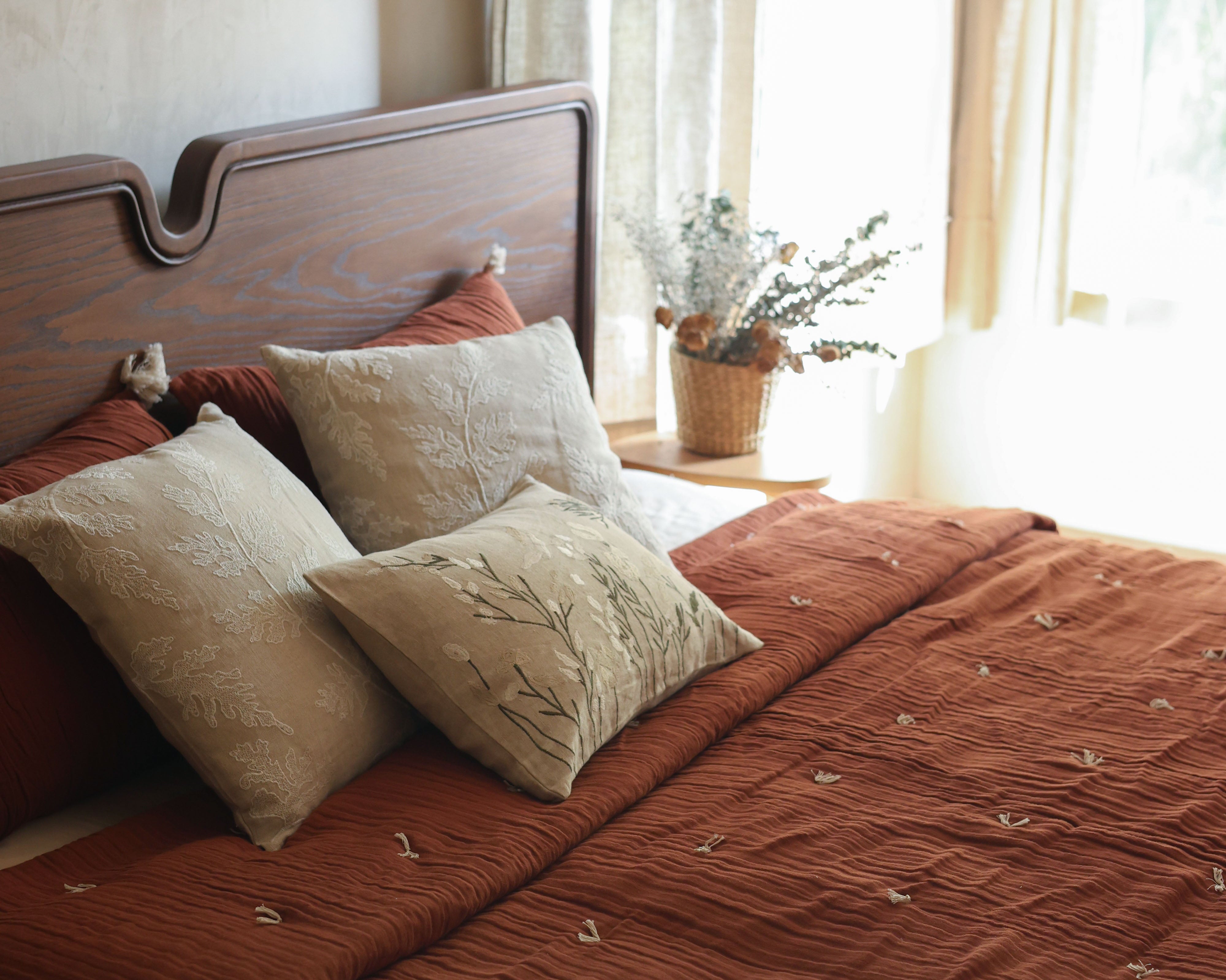 Bedroom styled with a Willow In Terracotta bedspread, cream cushions and a wooden headboard beside light curtains