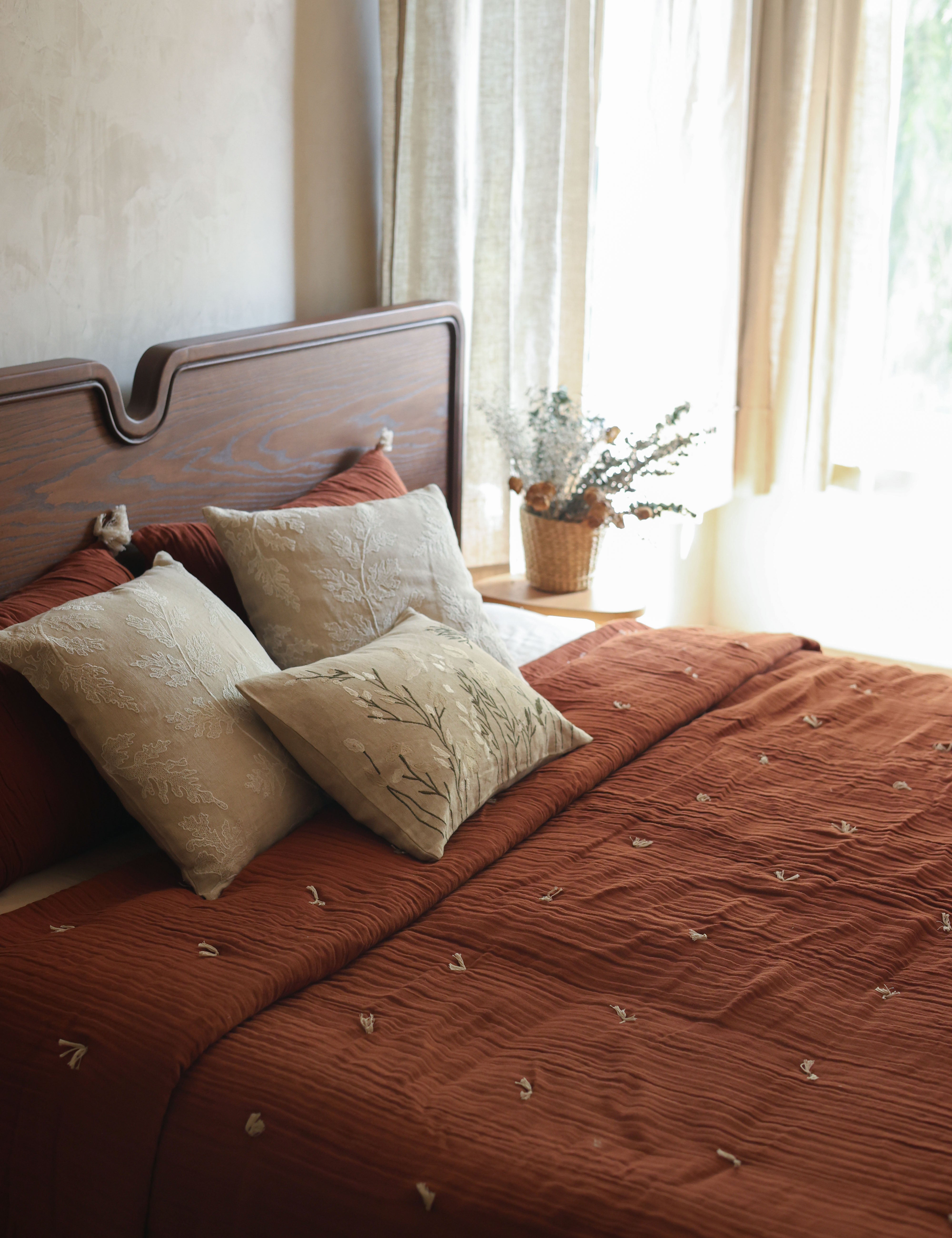 Bedroom styled with a Willow In Terracotta bedspread, cream cushions and a wooden headboard beside light curtains