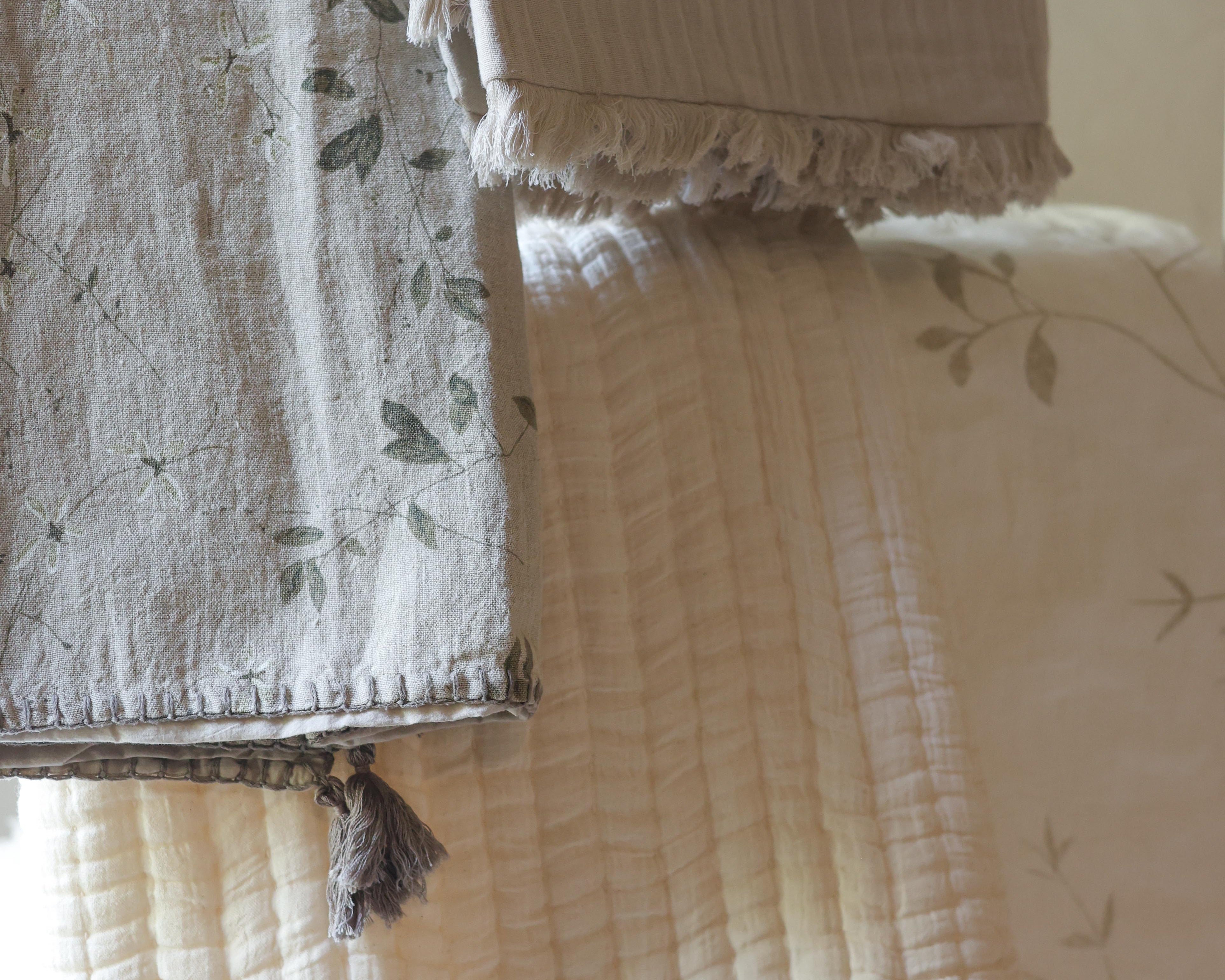 Neutral Aplito throws hanging in layers with floral patterns, textured fabric and tasselled edges