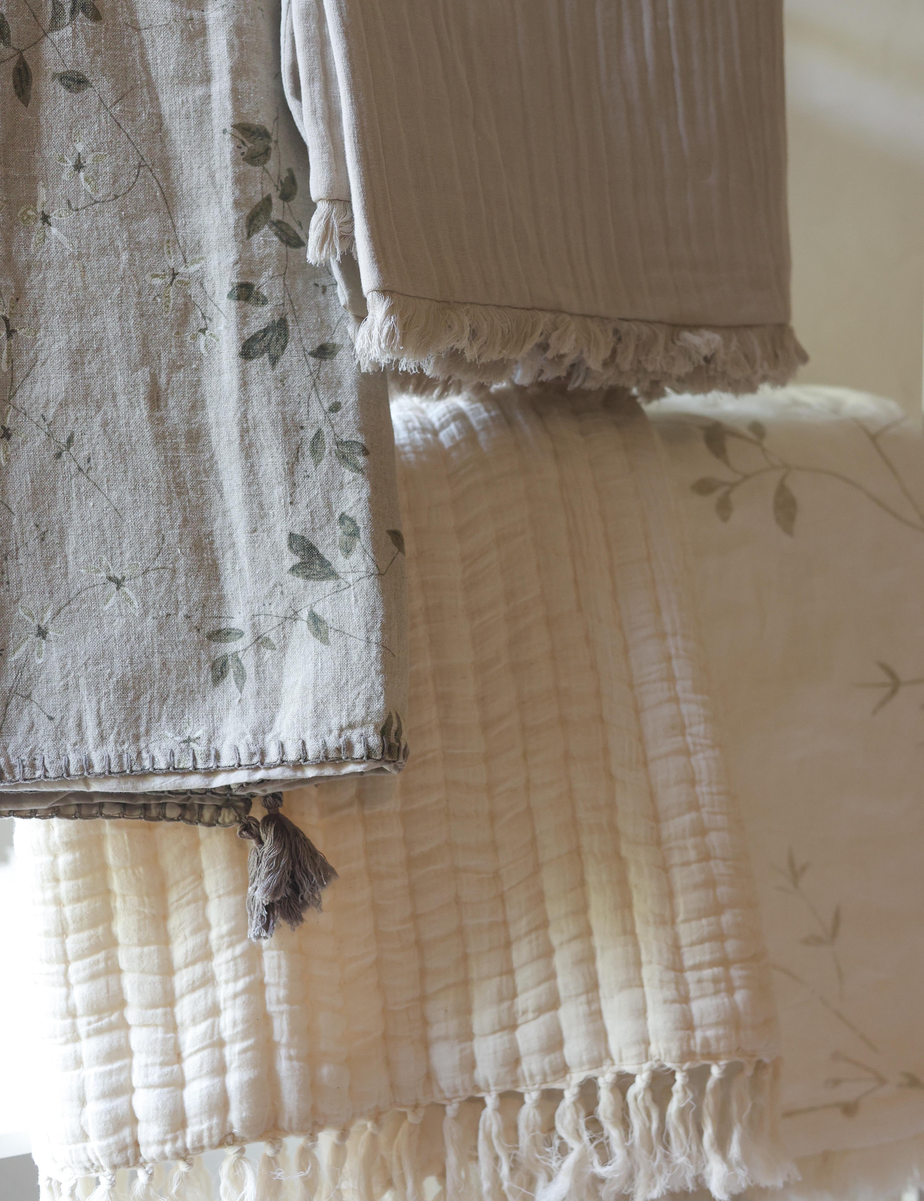 Neutral Aplito throws hanging in layers with floral patterns, textured fabric and tasselled edges