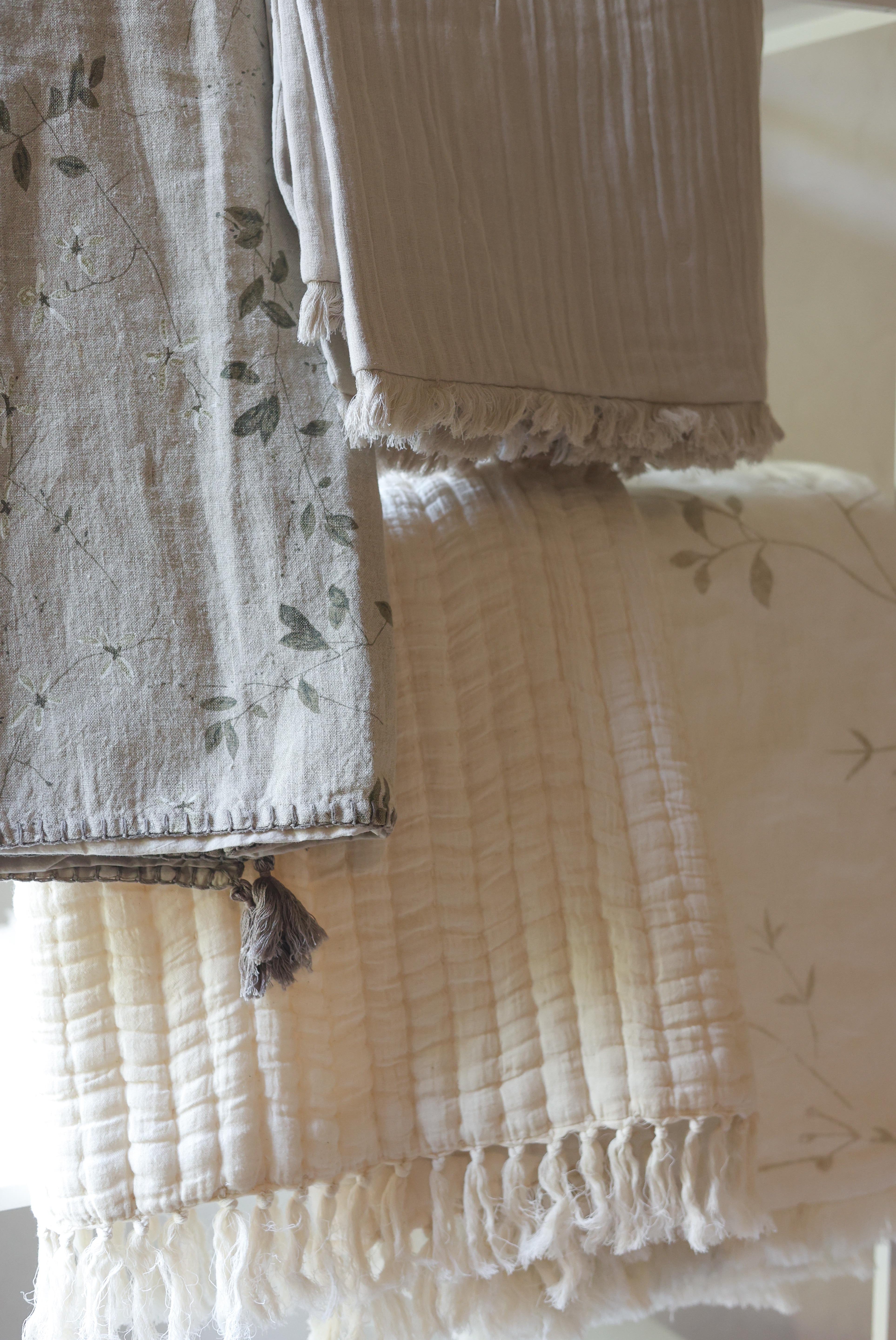 Neutral Aplito throws hanging in layers with floral patterns, textured fabric and tasselled edges